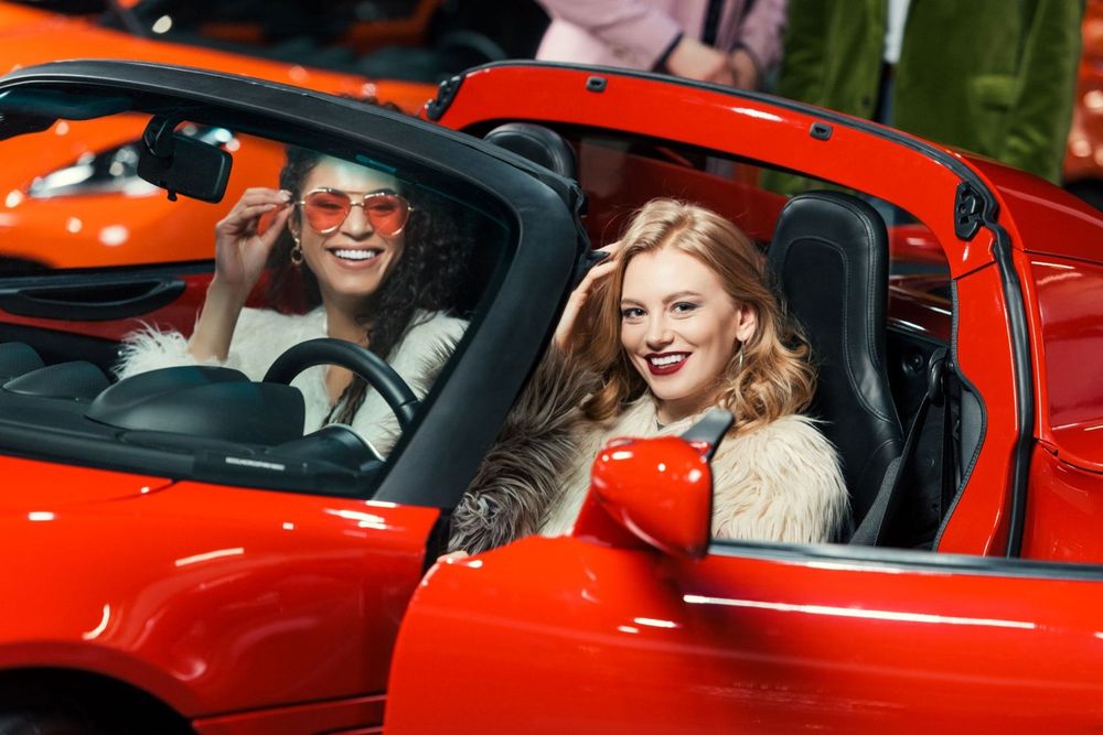 Two fashionable smiling multiethnic women sit in a Ferrari in Miami.